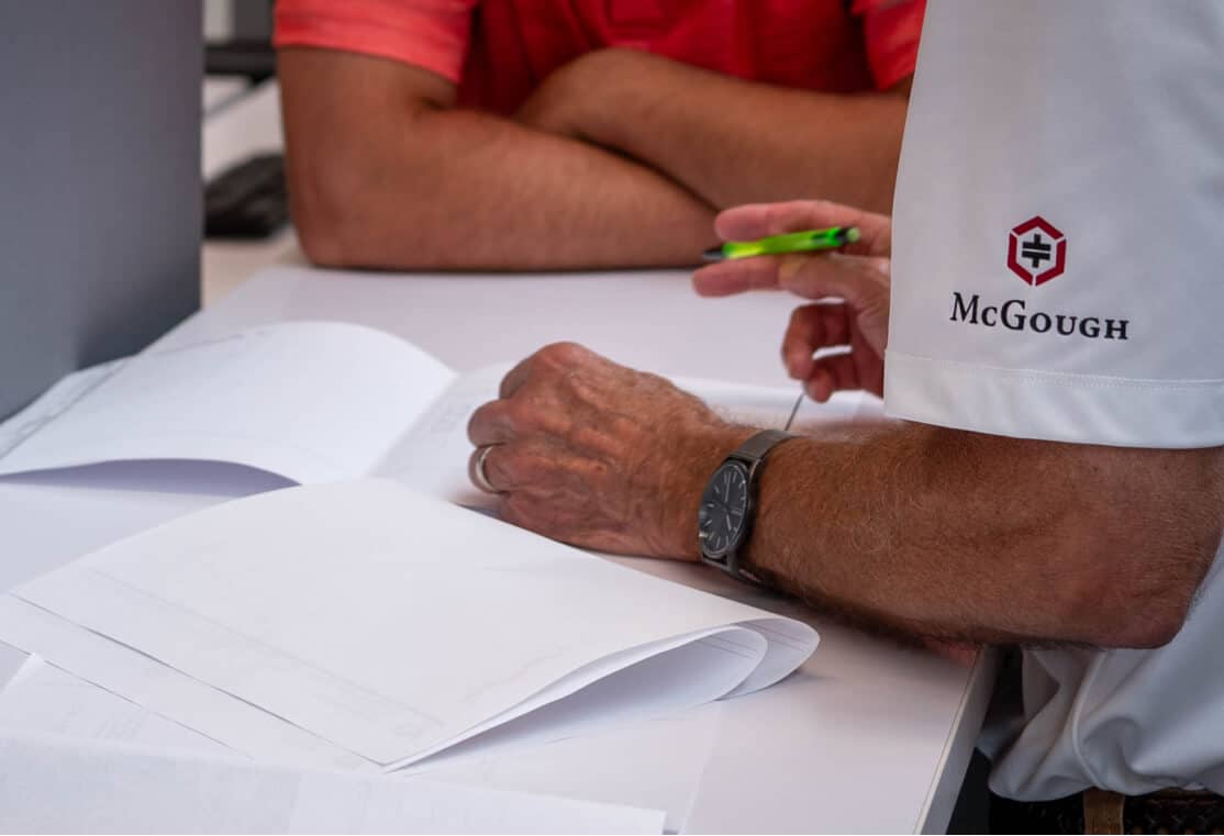 Two men looking over documents on a table, one wearing a McGough shirt