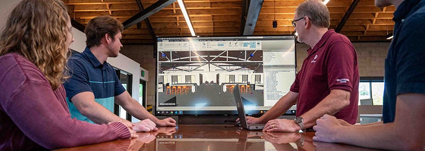 Four McGough project team members in an office looking at a rendering of a building