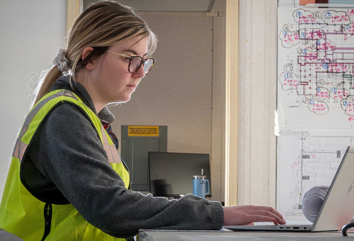 A female engineer in a yellow vest working on a computer on a McGough job site