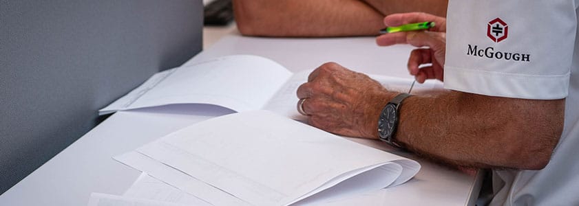 A man in a McGough shirt holding a pen, leaning over documents on a table