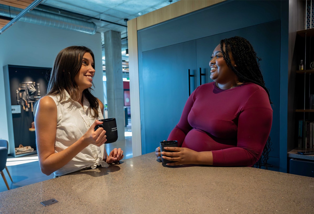 Two female McGough employees of diverse backgrounds working in an office, talking and smiling