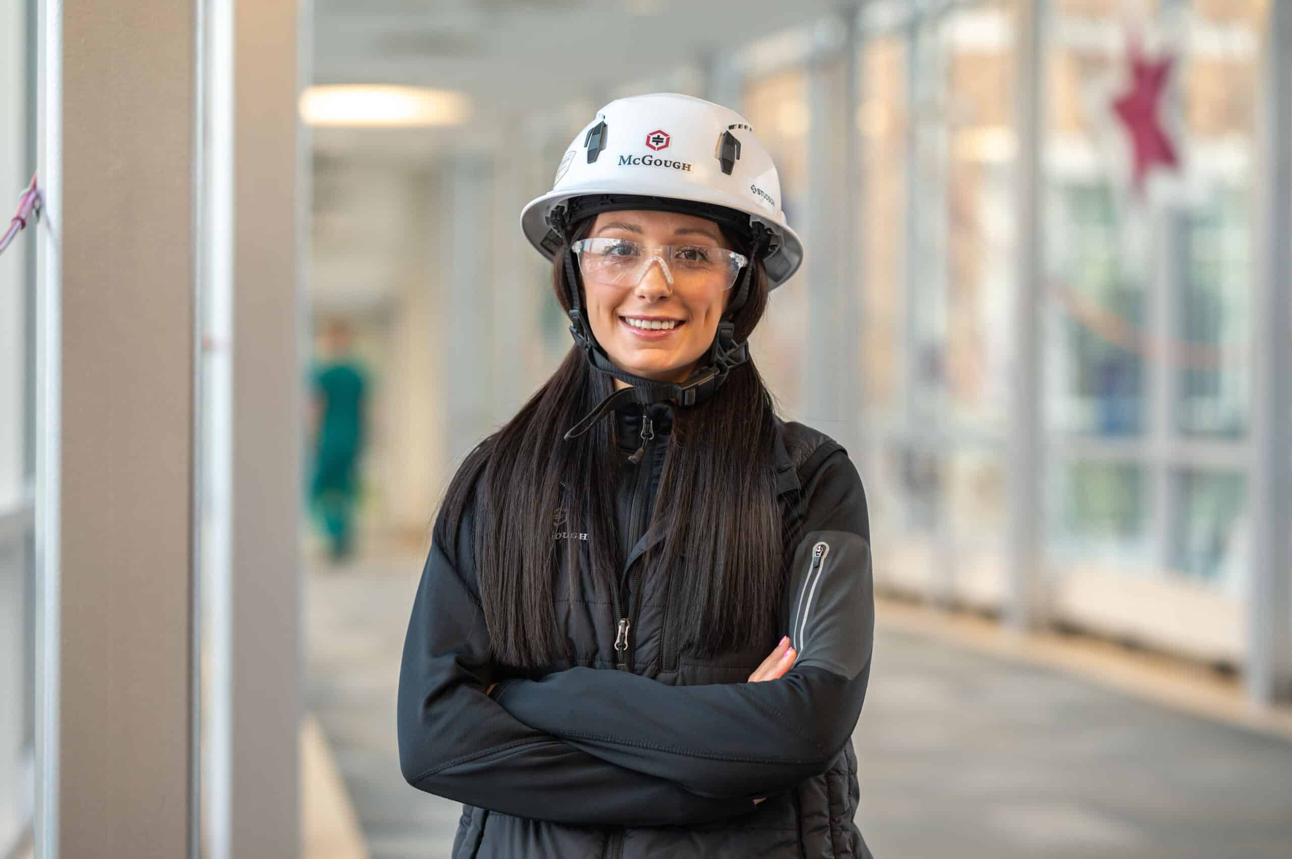A smiling woman in McGough safety gear on a job site holding a computer